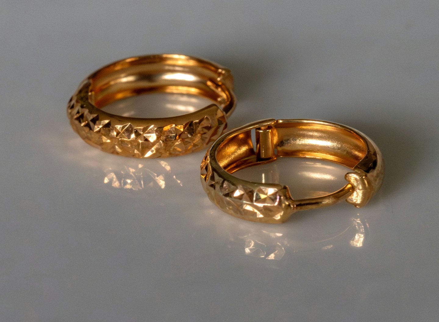 Two textured gold hoop earrings resting on a reflective surface.