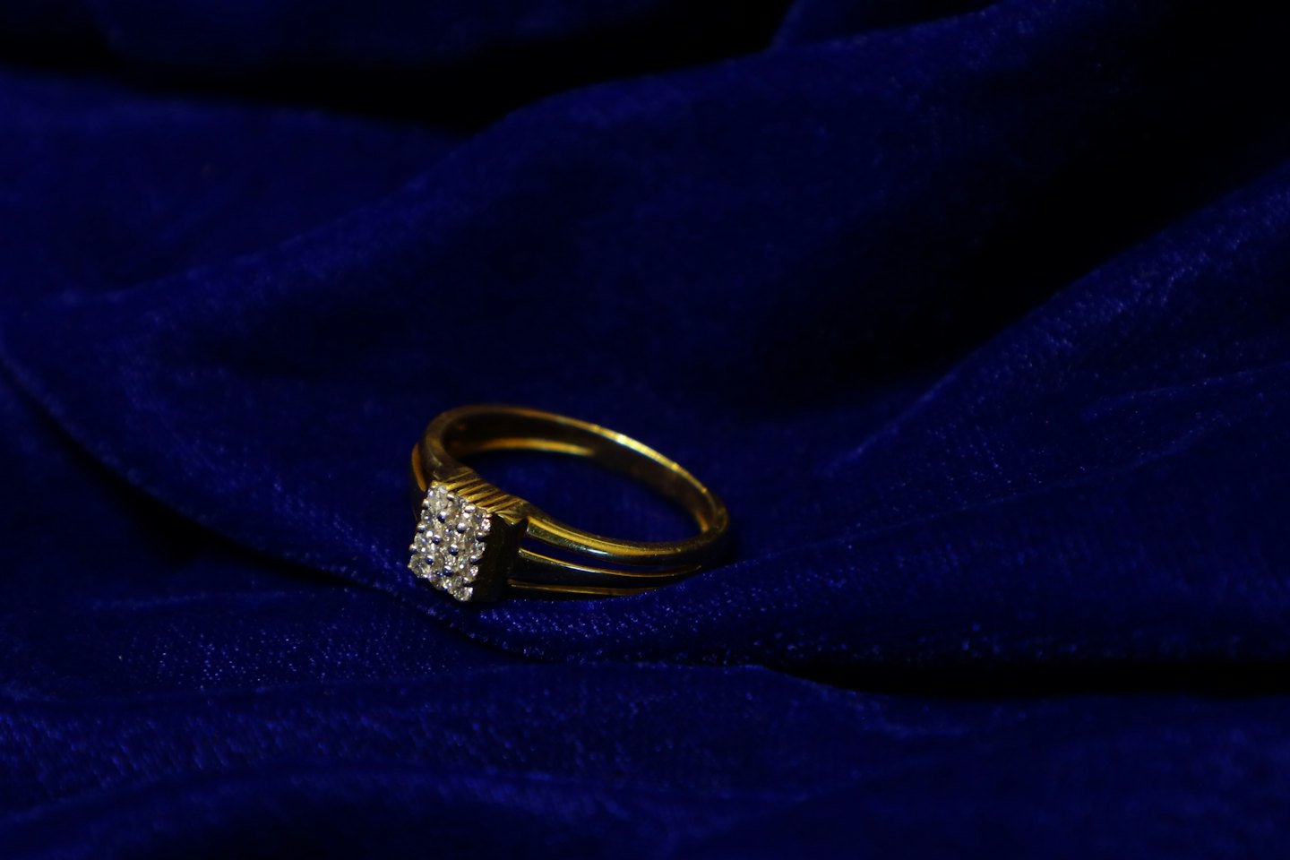 Gold ring with a diamond cluster resting on blue velvet.